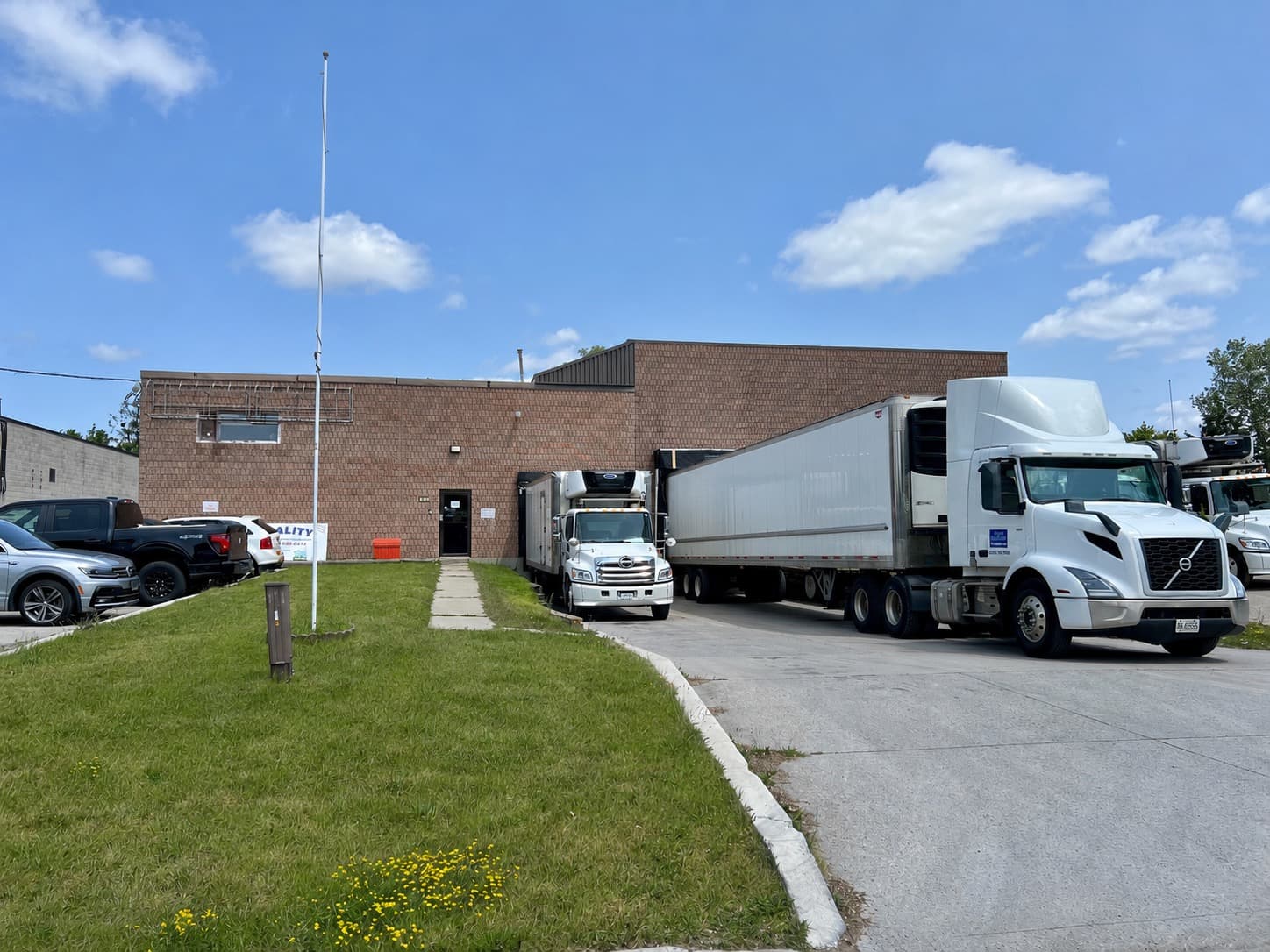 The exterior of the London Quality Dairy facility in London, Ontario, with refrigerated trucks parked outside on a sunny day.