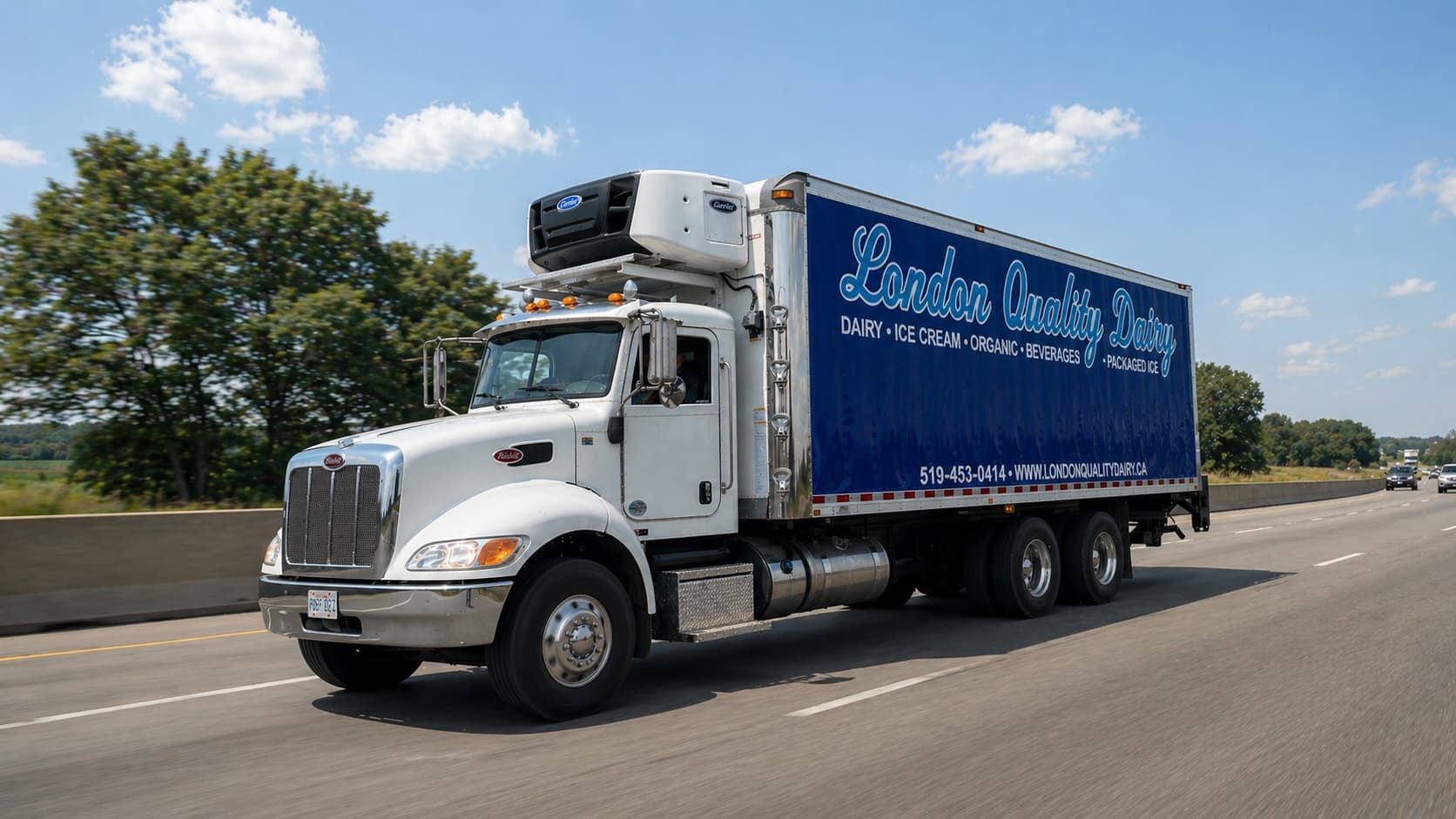 A London Quality Dairy refrigerated delivery truck travelling on a highway, its blue trailer lettered with dairy, ice cream, organic, beverages and packaged ice.